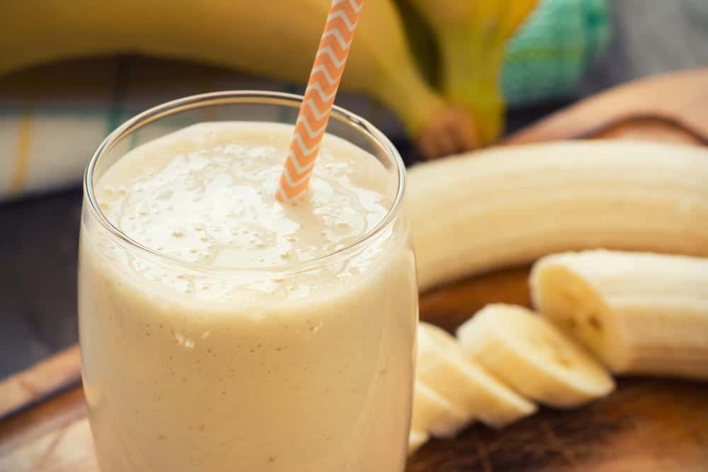 Banana smoothie in glass with straw, sliced banana in background