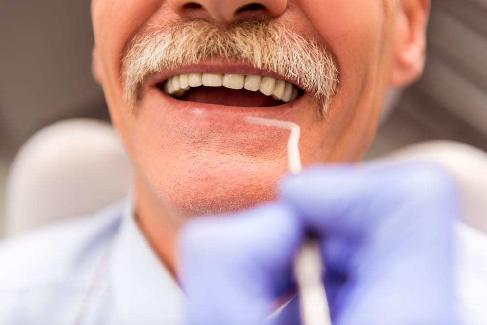 Close-up of smiling man wearing dentures as dentist uses dental tool