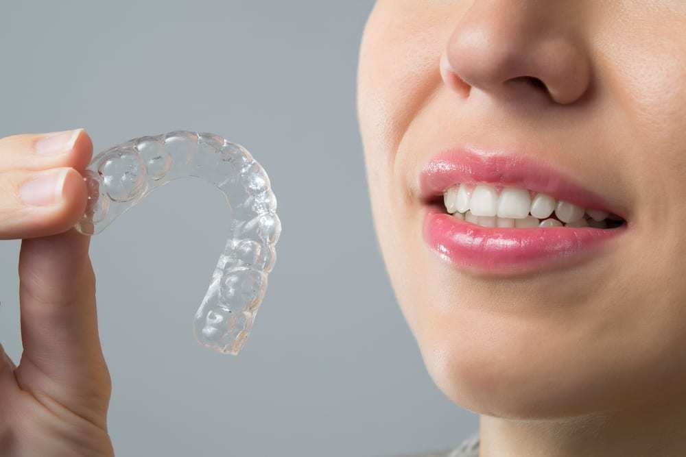 Close-up-of-woman-holding-clear-tooth-straitening-tray-near-mouth