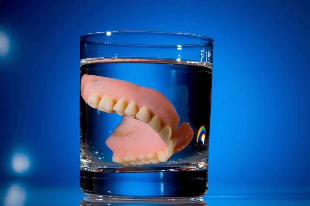 Dentures in glass of water, blue background