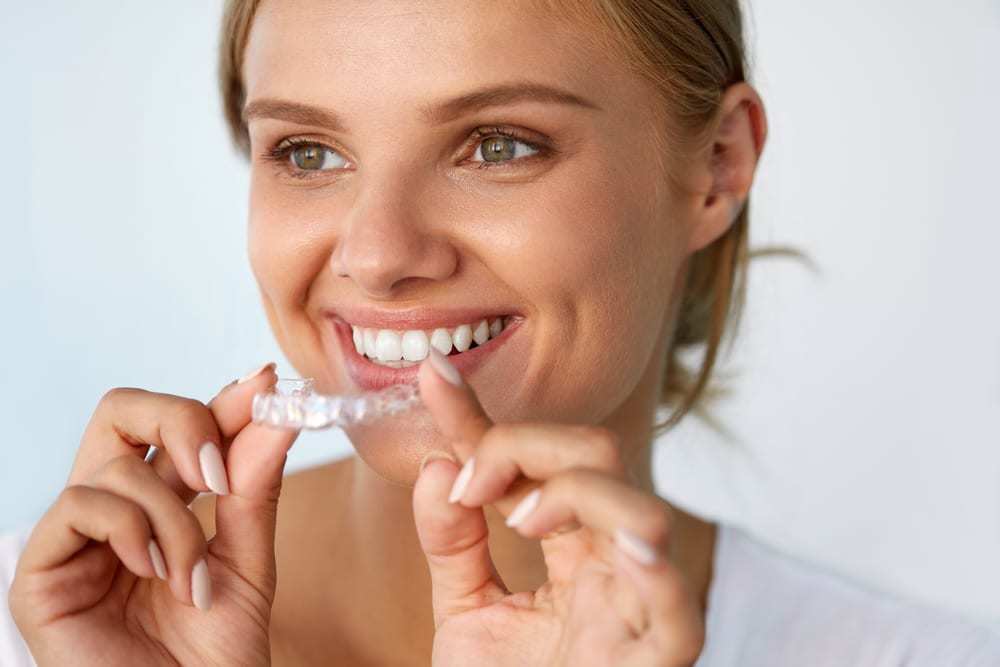 Woman with beautiful smile putting in invisalign aligner