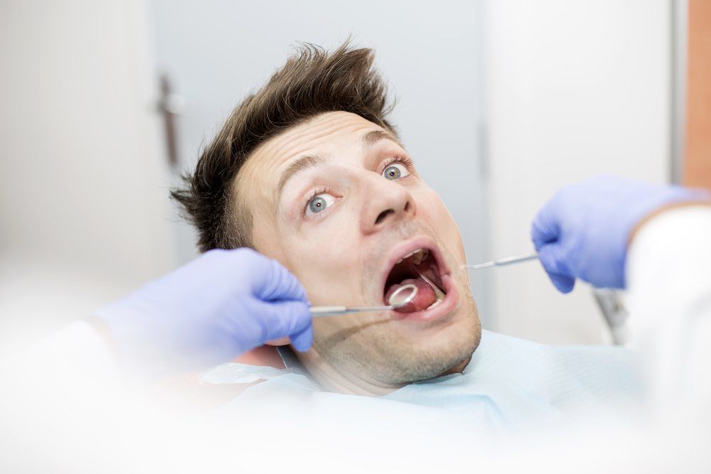 Scared young man at dentist office during teeth checkup
