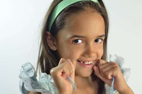 A closeup of a child flossing her teeth.