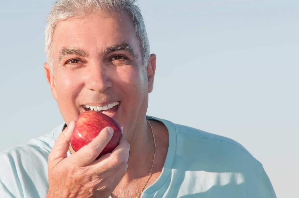 Smiling senior man biting into apple