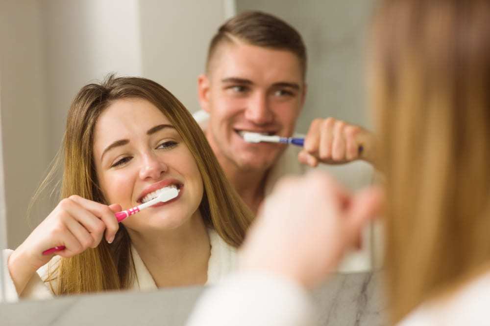 Young couple brushing their teeth in bathroom, looking at each other in mirror