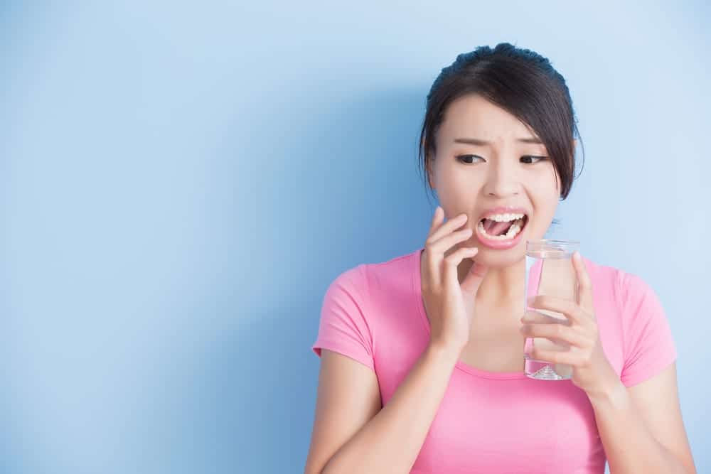 Woman drinking water, touching mouth and making face because her teeth are sensitive