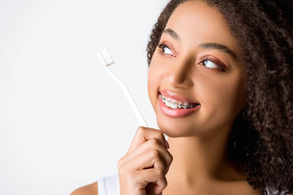 Young woman with braces, smiling, holding toothbrush