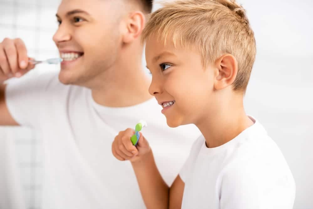 Smiling boy about to brush his teeth, looking at young man brushing his teeth