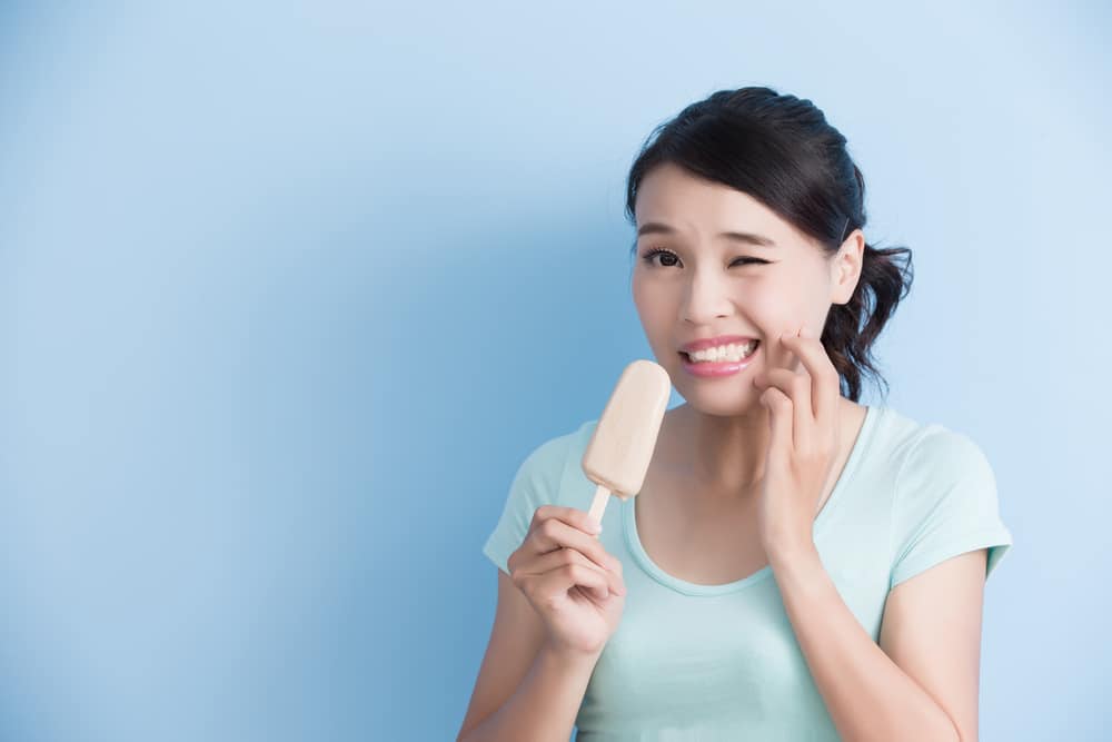 Young woman with sensitive teeth eating ice cream bar