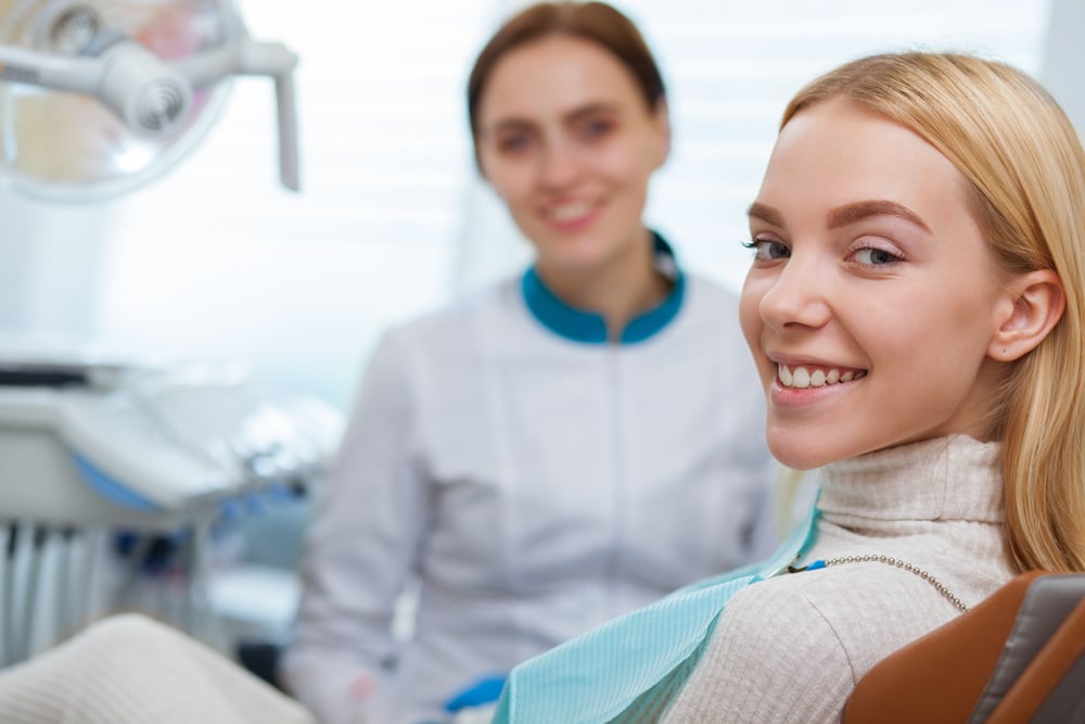 Young woman smiling while sitting in dentist's chair, dentist in background