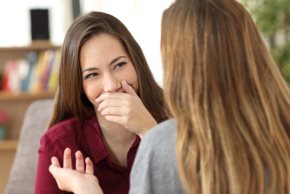 Woman covering mouth while talking to another woman