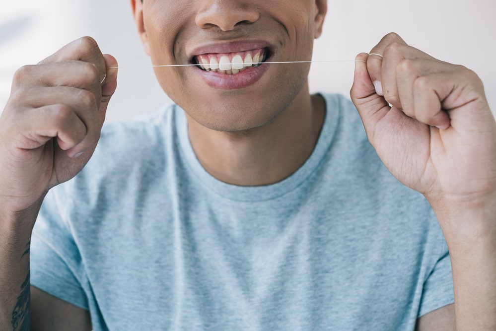 Close-up of smiling young man flossing teeth