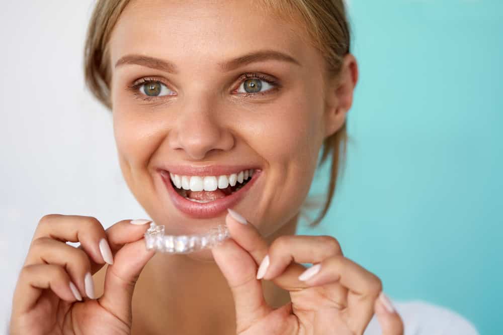 Smiling young woman inserting invisalign aligner to straighten teeth