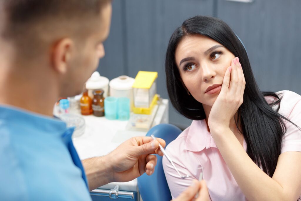 Young woman holding hand to cheek, looking at dentist